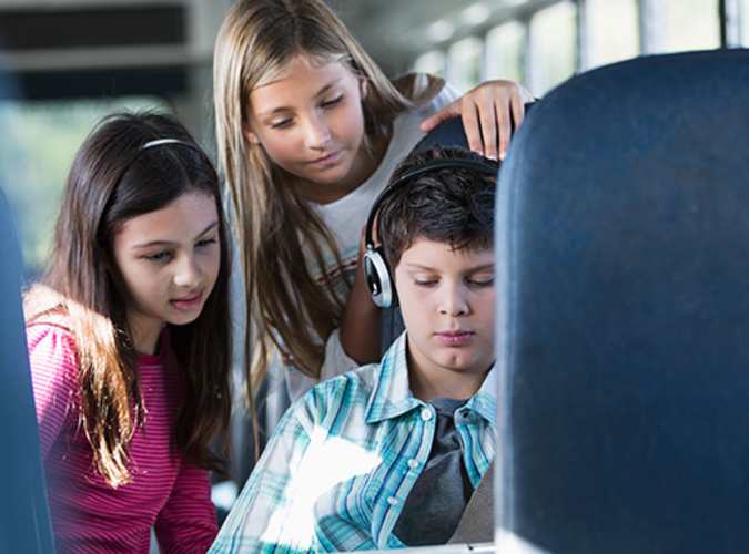 Three children on a bus looking at a tablet.